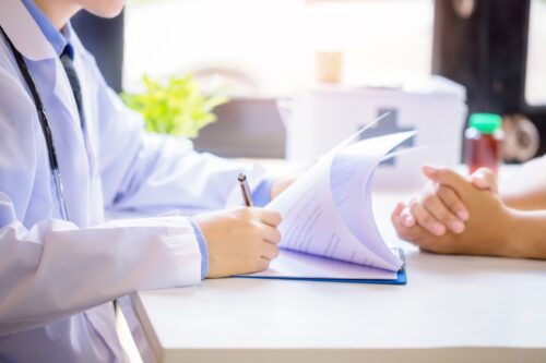 doctor man consulting patient while filling up an application form at the desk in hospital
